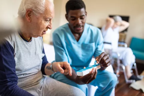 Een verpleegster laat een bejaarde zien hoe je een medicijndoosje gebruikt