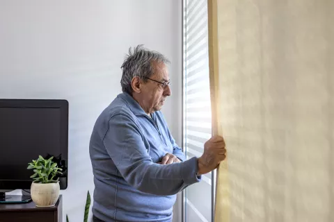 Een oudere persoon kijkt uit een raam